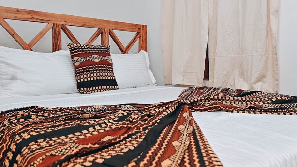 A bed with a wooden headboard, white pillows, and a patterned throw blanket.