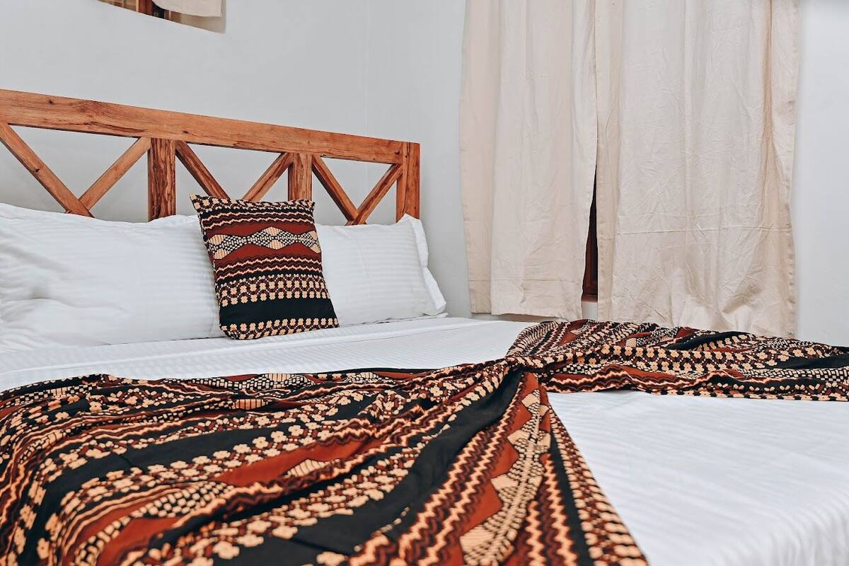 Una cama con cabecera de madera, almohadas blancas y una manta estampada.