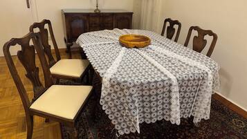 A dining area with a table covered in a lace tablecloth, surrounded by wooden chairs with cushioned seats.