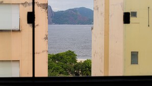 A view through a window of a building with a large body of water and a mountain in the background. - SUH Flamengo 08 Live in Aterro (Rio de Janeiro)