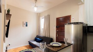 A compact kitchen with a refrigerator, a dining area with a table set for two, a sofa, and a window with curtains. - SUH Flamengo 08 Live in Aterro (Rio de Janeiro)