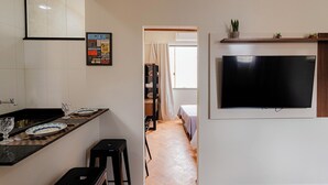 A modern kitchen with a black countertop, a large flat-screen TV mounted on the wall, and a wooden shelf above the TV. - SUH Flamengo 08 Live in Aterro (Rio de Janeiro)
