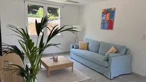 A modern living room with a light blue sofa, a wooden coffee table, and a large potted plant. - Family villa with a pool, 100 meters from the beach – Le Lavandou (Le Lavandou)