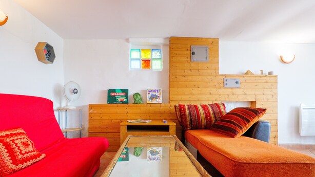 Une pièce chaleureuse avec un canapé rouge, une petite table et un mur en bois doté d’une fenêtre.