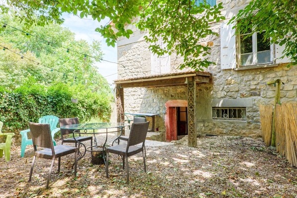 An outdoor patio with wicker chairs and a glass table, surrounded by stone walls and greenery.