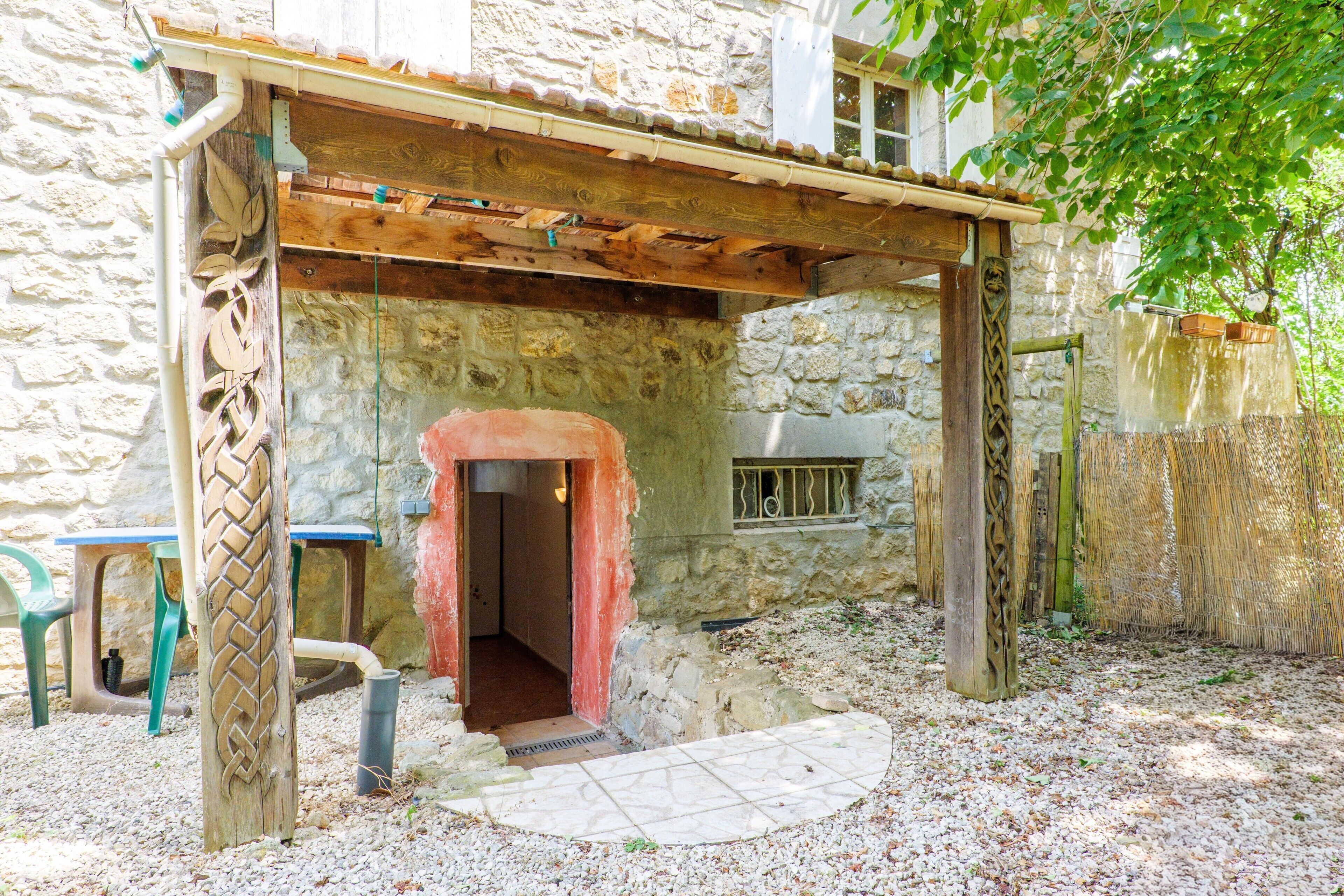 A stone building with a wooden pergola entrance, a small window, and a door leading inside.