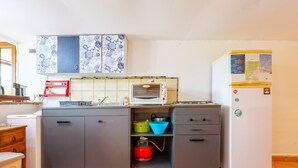 Une cuisine avec des meubles gris, un réfrigérateur blanc, une cuisinière à gaz et un four à micro-ondes.