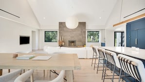 Una cucina moderna con una grande isola, un'area pranzo con tavolo e sedie in legno, e un soggiorno con divano e camino.