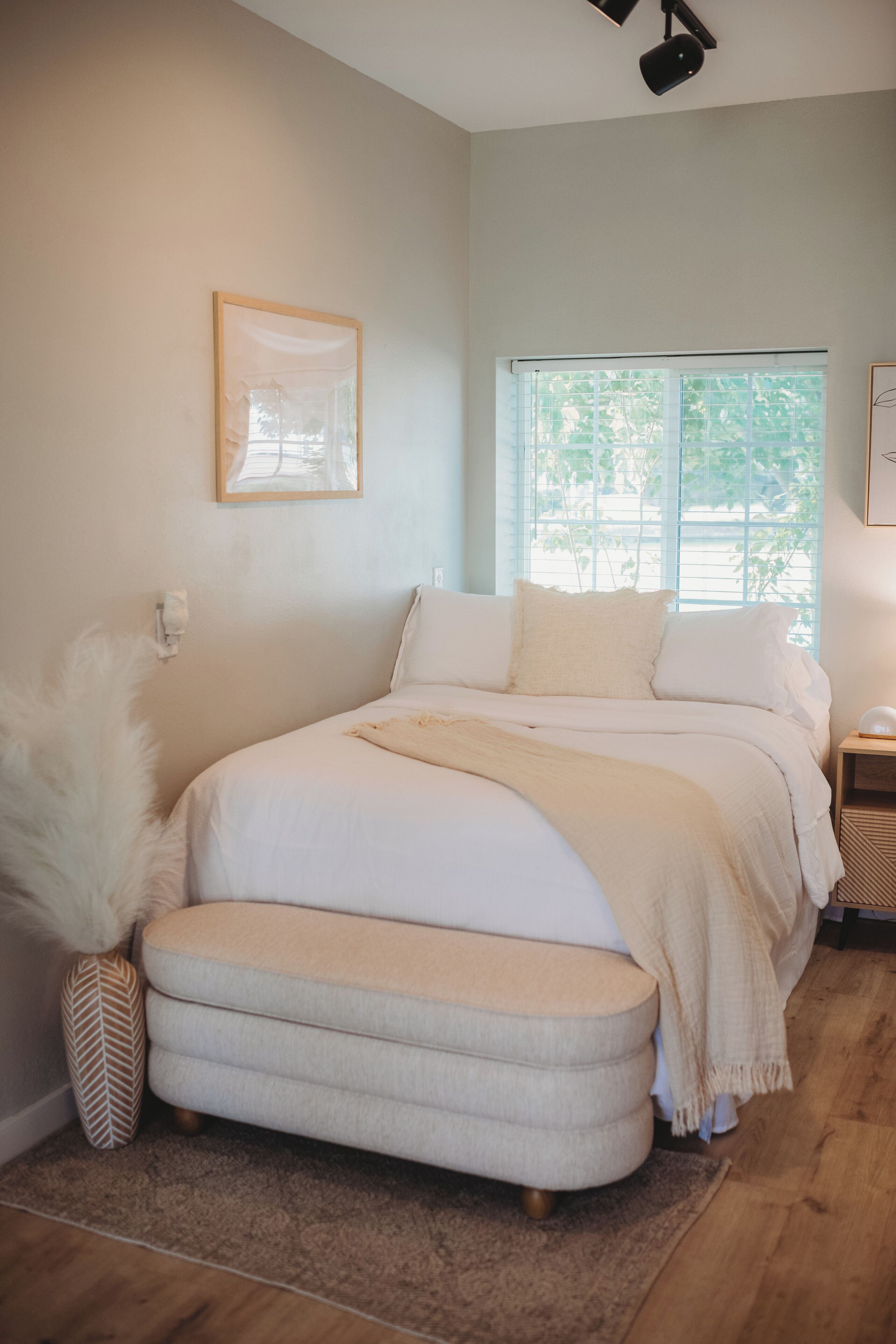 A bedroom with a bed, a bedside table, a window, and a wall-mounted light fixture.