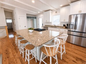 Una cocina con una isla grande, taburetes blancos de bar, electrodomésticos de acero inoxidable y suelo de madera.