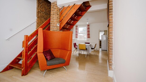 A modern interior with a wooden staircase, a red chair, and a dining area.