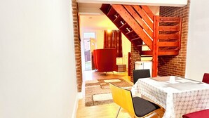 A dining area with a table set for four, a yellow chair, and a red chair. A wooden staircase with a black railing is visible in the background.
