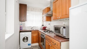 A compact kitchen with wooden cabinets, a washing machine, a stove, and a microwave.