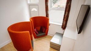 A room with two orange armchairs, a small table, and a television mounted on the wall.