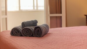 Una cama bien hecha con colcha rosa y toallas enrolladas encima.