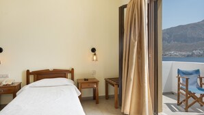 A hotel room with a bed, bedside table, lamp, and a view of a balcony with a chair.
