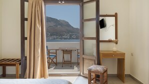 Una habitación con cama, escritorio, silla, una mesita y vistas a una montaña y al agua.