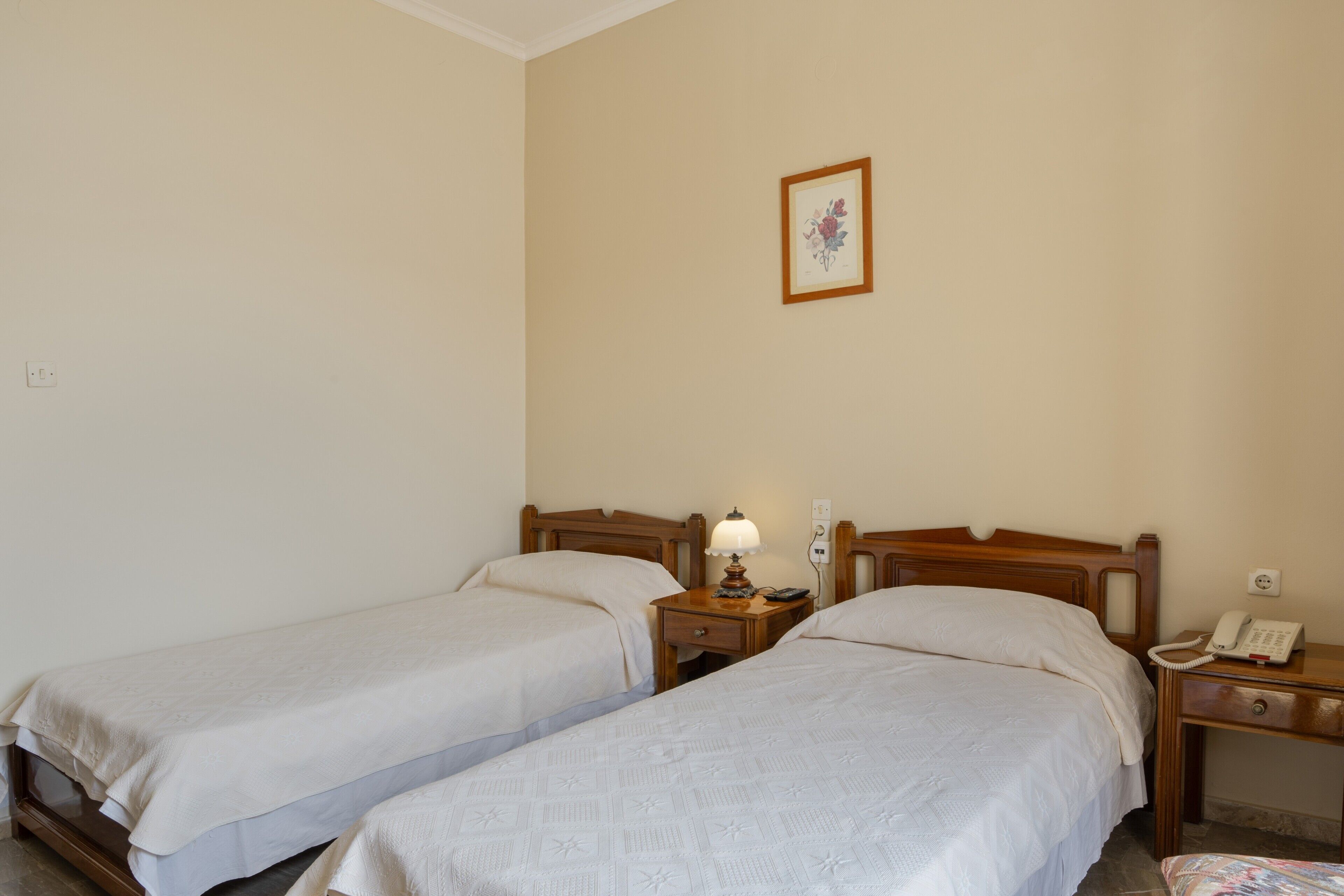 Une chambre avec deux lits simples, des tables de chevet, une lampe, un téléphone et un tableau encadré au mur.