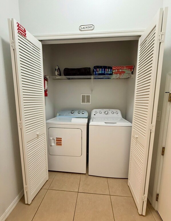 A laundry room with two dryers, a shelf with folded clothes, and a fire extinguisher. - Corner Resort Luxe 4BR 3BA with Private Pool Near Parks (Kissimmee)