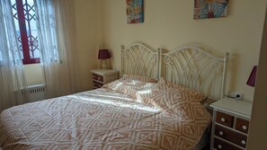 A bedroom with a patterned bedspread, a white metal headboard, a bedside table with a lamp, and a small dresser. - Casares Costa, Vista Bahia,2 Bedroom Bathroom (Casares)