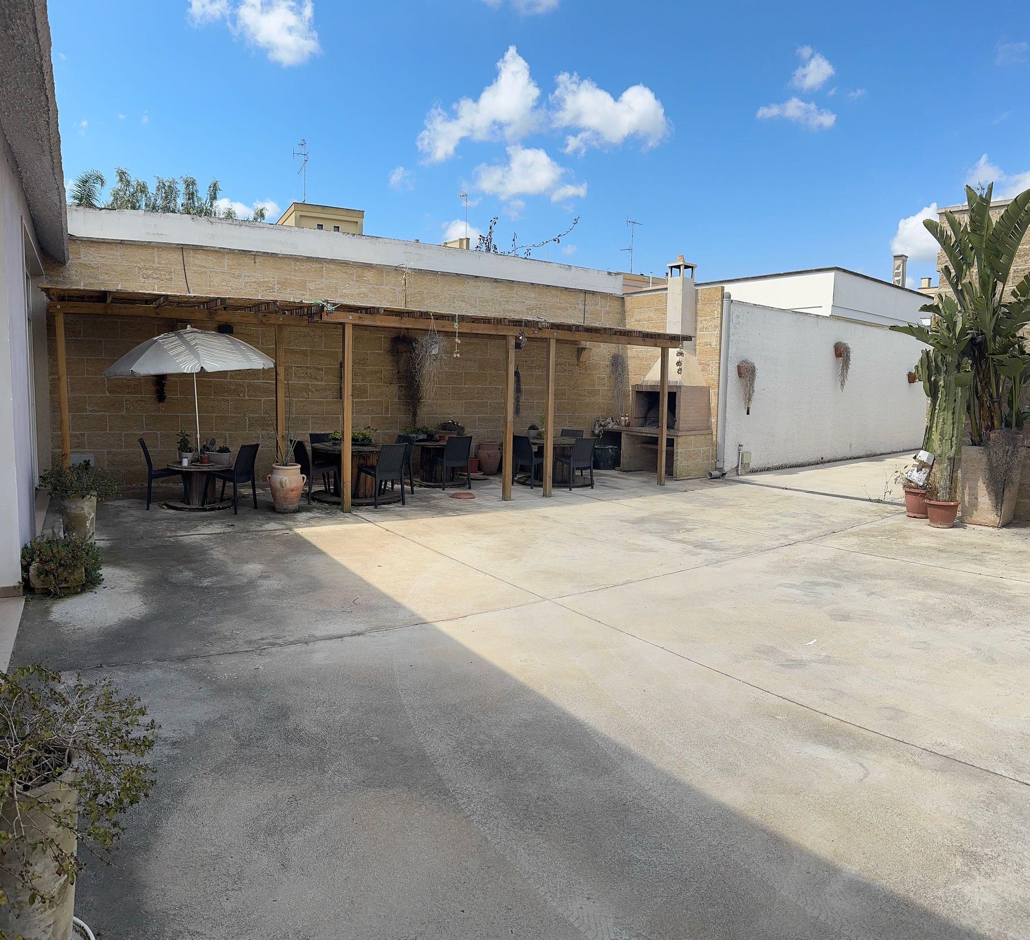 An outdoor patio area with a brick wall, a wooden pergola, and a pizza oven.