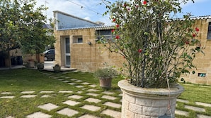 A garden with a stone pathway, a large planter with a rose bush, and a building with a tiled roof. - Dear Mary B&B (San Cesario di Lecce)