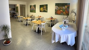 A dining area with tables and chairs, a kitchen in the background, and artwork on the walls. - Dear Mary B&B (San Cesario di Lecce)