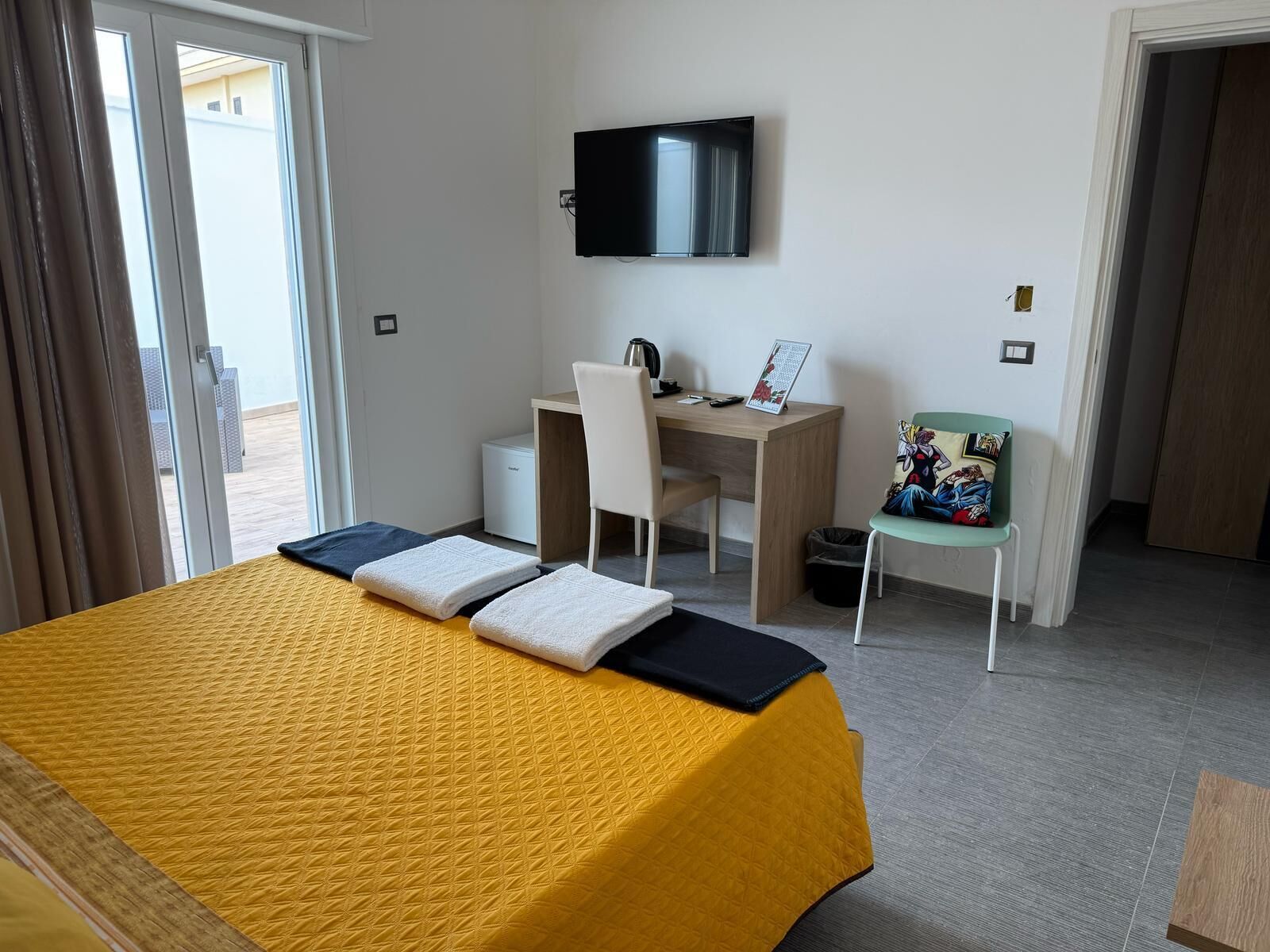 A hotel room with a bed, a desk, a chair, a television, and a view of the outside.