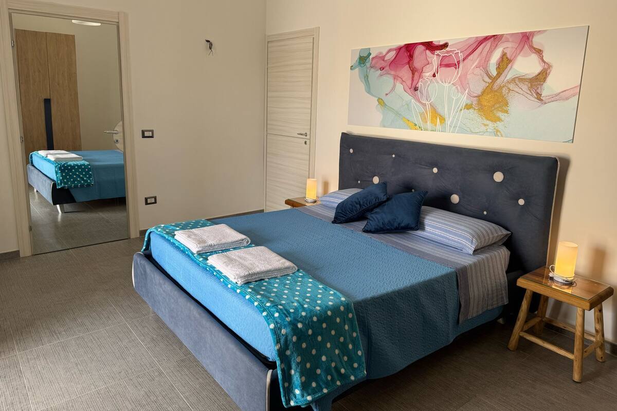 Un dormitorio ordenado con una cama grande, una mesita de noche con lámpara y un espejo.