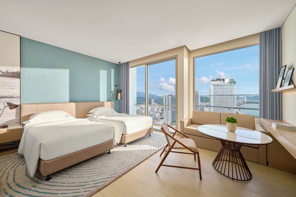 A modern hotel room with two beds, a sofa, a round table, and a large window offering a city view. - Hyatt Regency Nha Trang (Nha Trang)