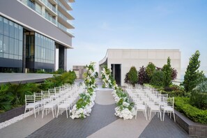 An outdoor wedding venue with white chairs arranged in rows, a floral aisle, and modern buildings in the background. - Hyatt Regency Nha Trang (Nha Trang)