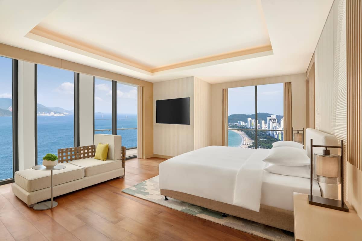 A modern hotel room with a large bed, a sofa, a TV, and a city view.