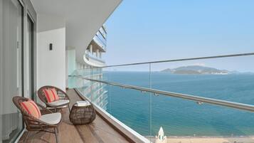 Ein Balkon mit Korbstühlen, einem kleinen Tisch und Blick auf das Meer und das entfernte Land.