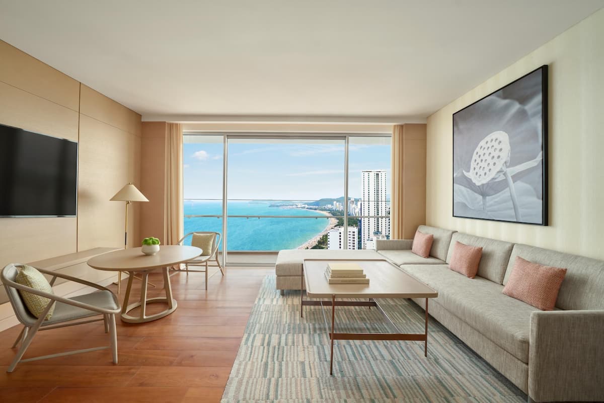 A modern hotel room with a balcony, a sofa, a dining table, and a TV.