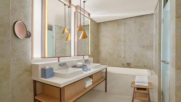 A modern bathroom with a double sink vanity, a large mirror, pendant lights, a bathtub, and a small wooden stool.