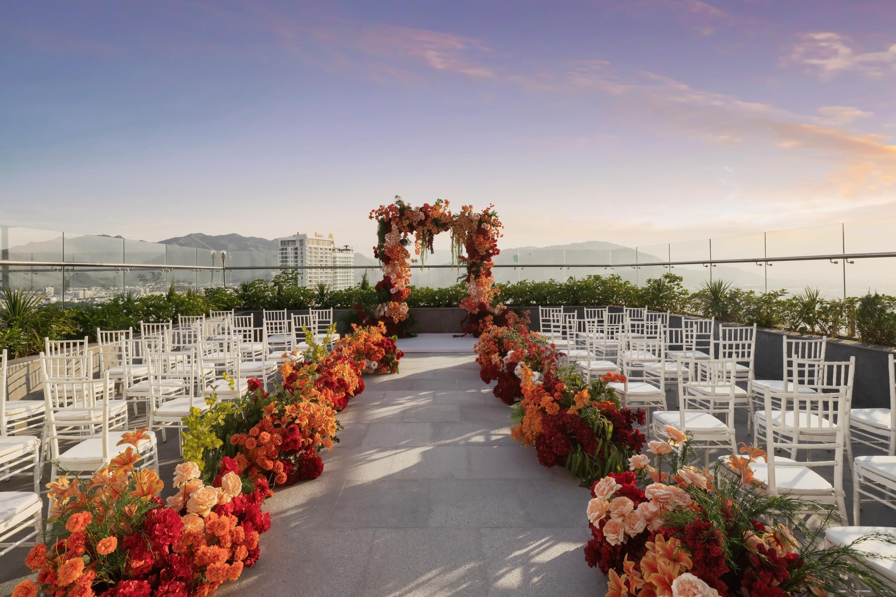 An outdoor event space with a floral archway, white chairs, and a clear view of the cityscape in the background.