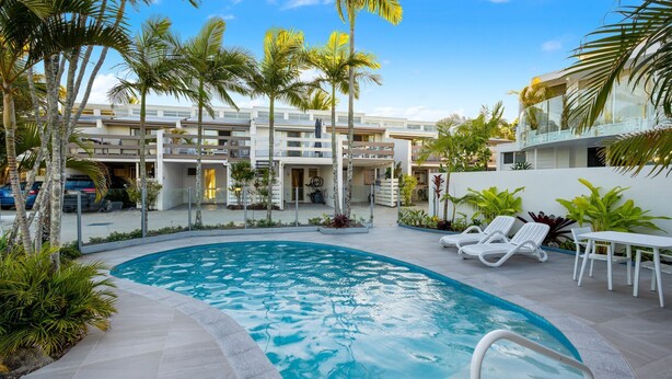 Un área de piscina con jacuzzi, sillones de descanso y palmeras.