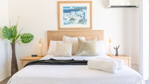 Una cama bien tendida con sábanas blancas, cabecera de madera y un cuadro enmarcado encima.