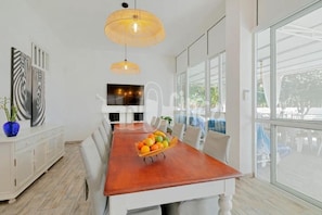 A modern dining area with a wooden table, white chairs, and a fruit basket.