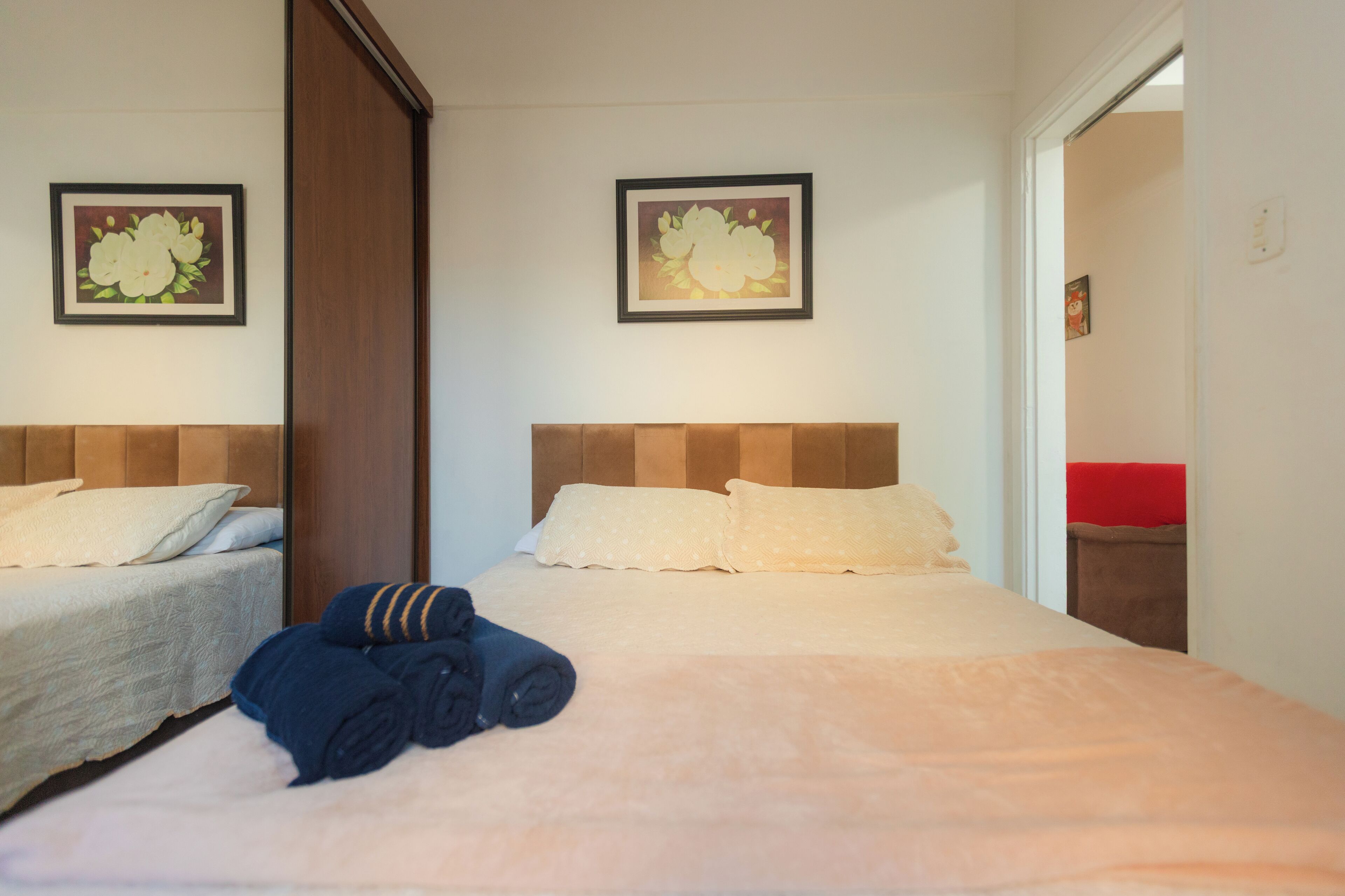 Een hotelkamer met twee bedden, elk met hoofdbord, een groot bed met een beige sprei, en twee ingelijste bloemschilderijen aan de wanden.