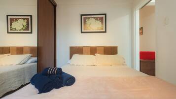 Een hotelkamer met twee bedden, elk met hoofdbord, een groot bed met een beige sprei, en twee ingelijste bloemschilderijen aan de wanden.