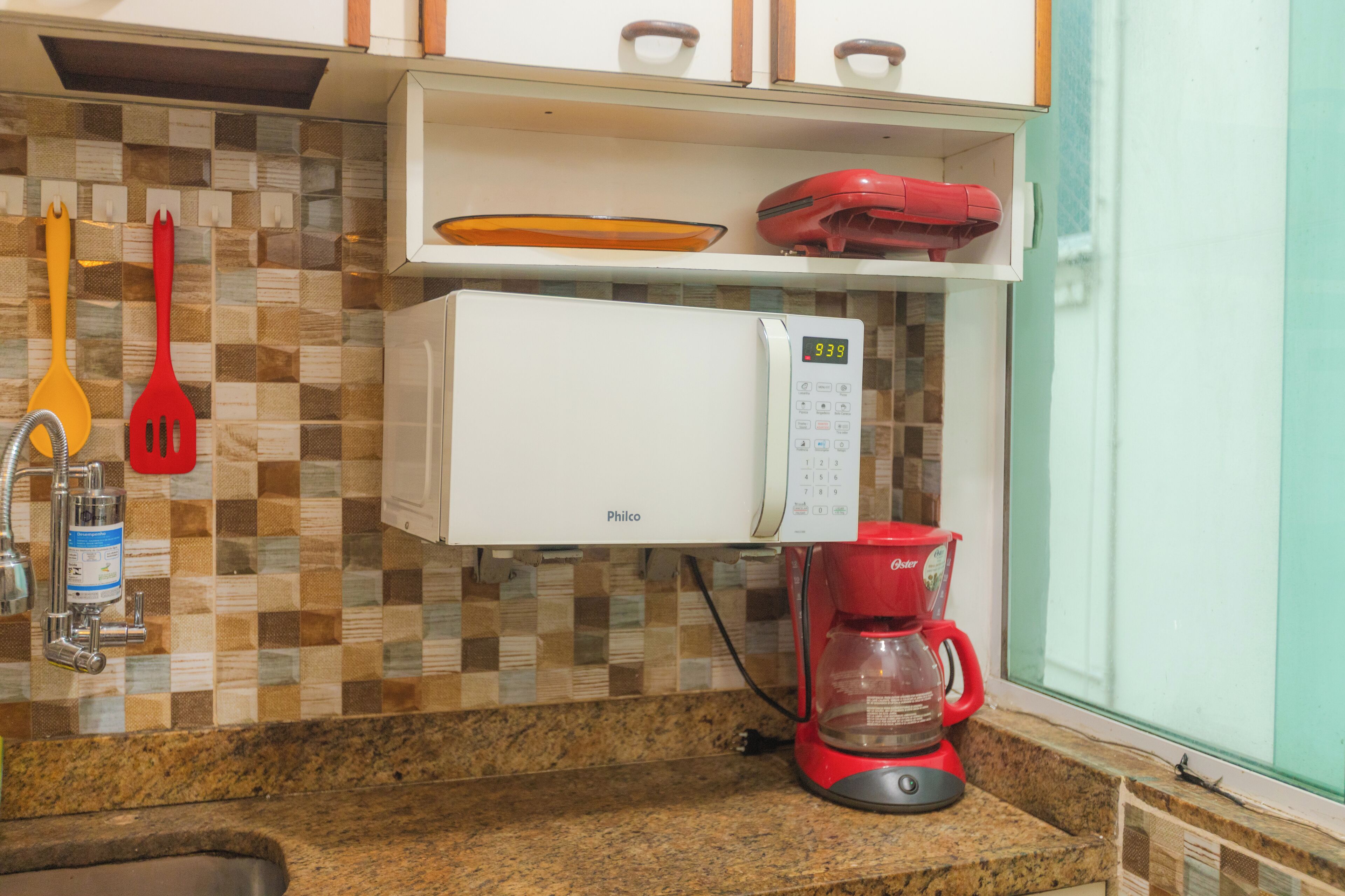 Uma cozinha com micro-ondas, cafeteira e painel de parede xadrez.