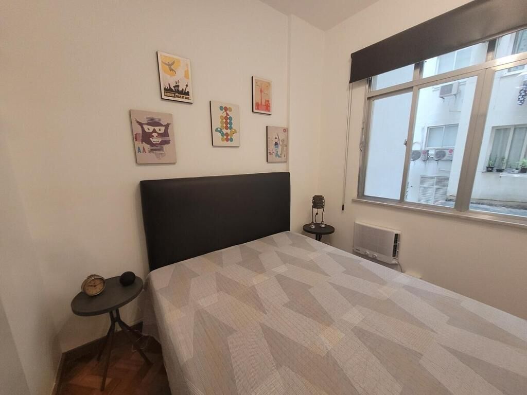 Un dormitorio con cama, una mesita y una ventana.
