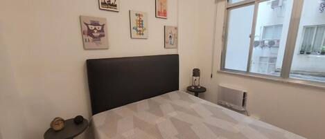 Un dormitorio con cama, una mesita y una ventana.