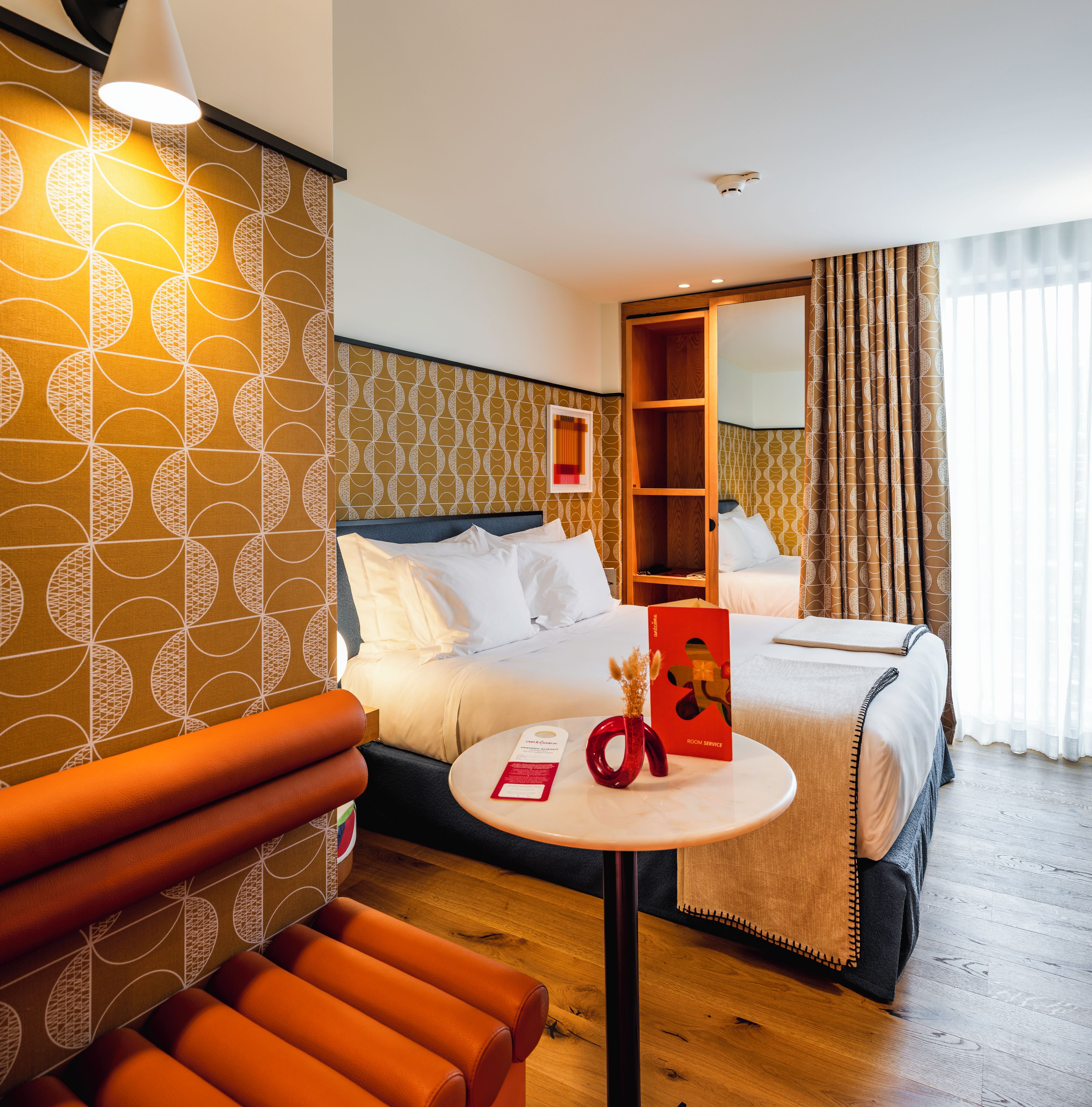 A hotel room with a bed, a bedside table, a chair, and a mirror.