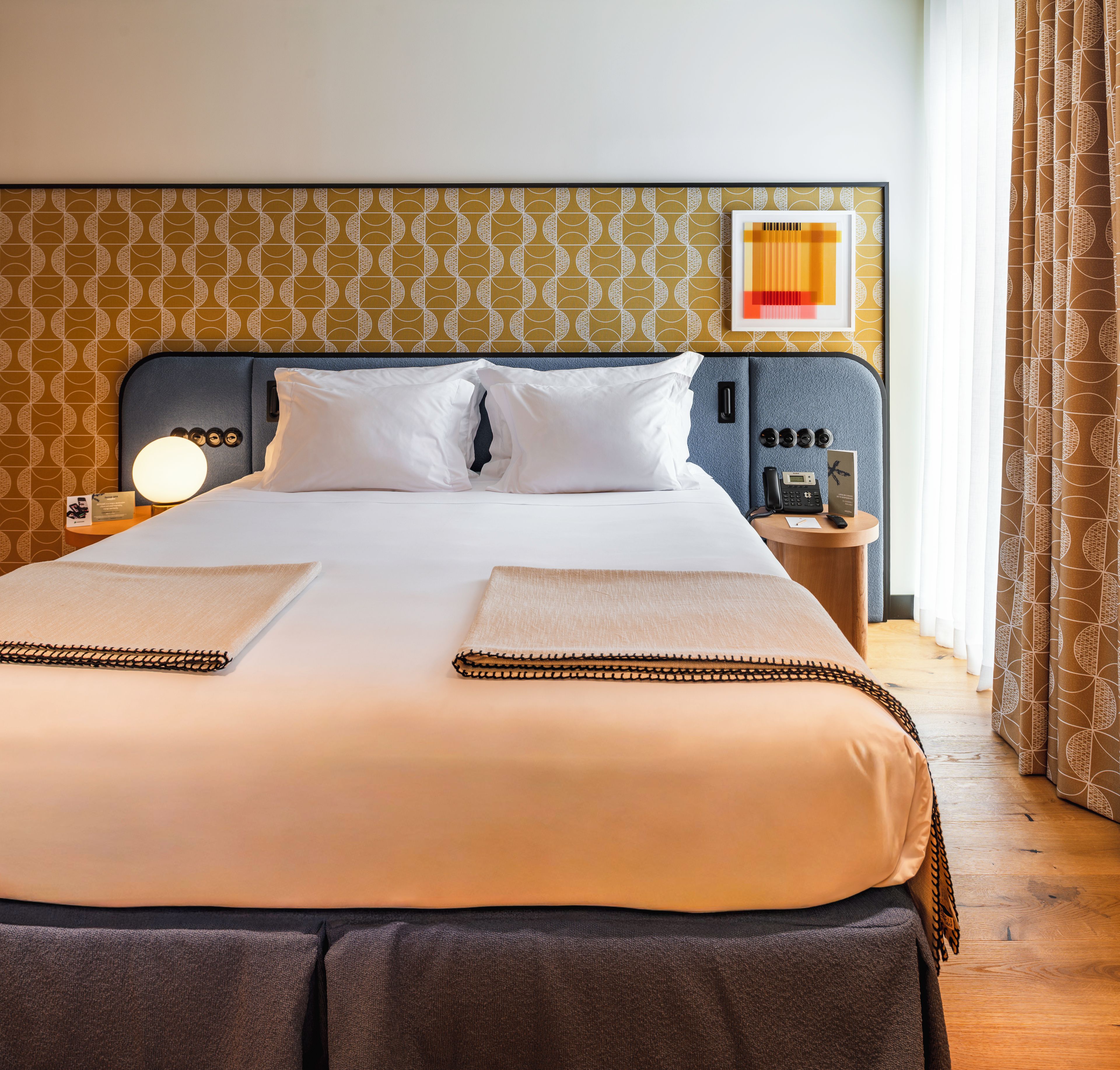 Une chambre d’hôtel équipée d’un lit, d’une table de chevet, d’un téléphone et d’une lampe fixée au mur.