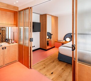 A modern hotel room with a wooden wardrobe, a bed with a headboard, a bedside table with a lamp, and a flat-screen TV mounted on the wall. - Artcore Hotel Porto (Porto)