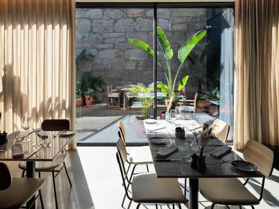 A modern dining area with a glass table and chairs, a stone wall, and potted plants.