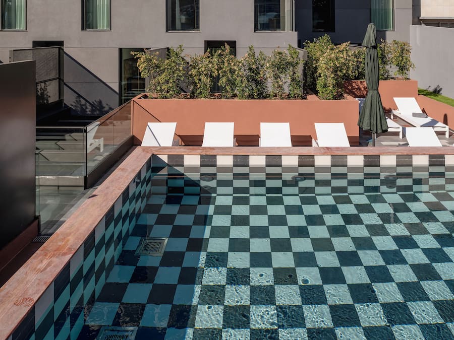 A rooftop pool with checkered tiles, white lounge chairs, and a glass balustrade.