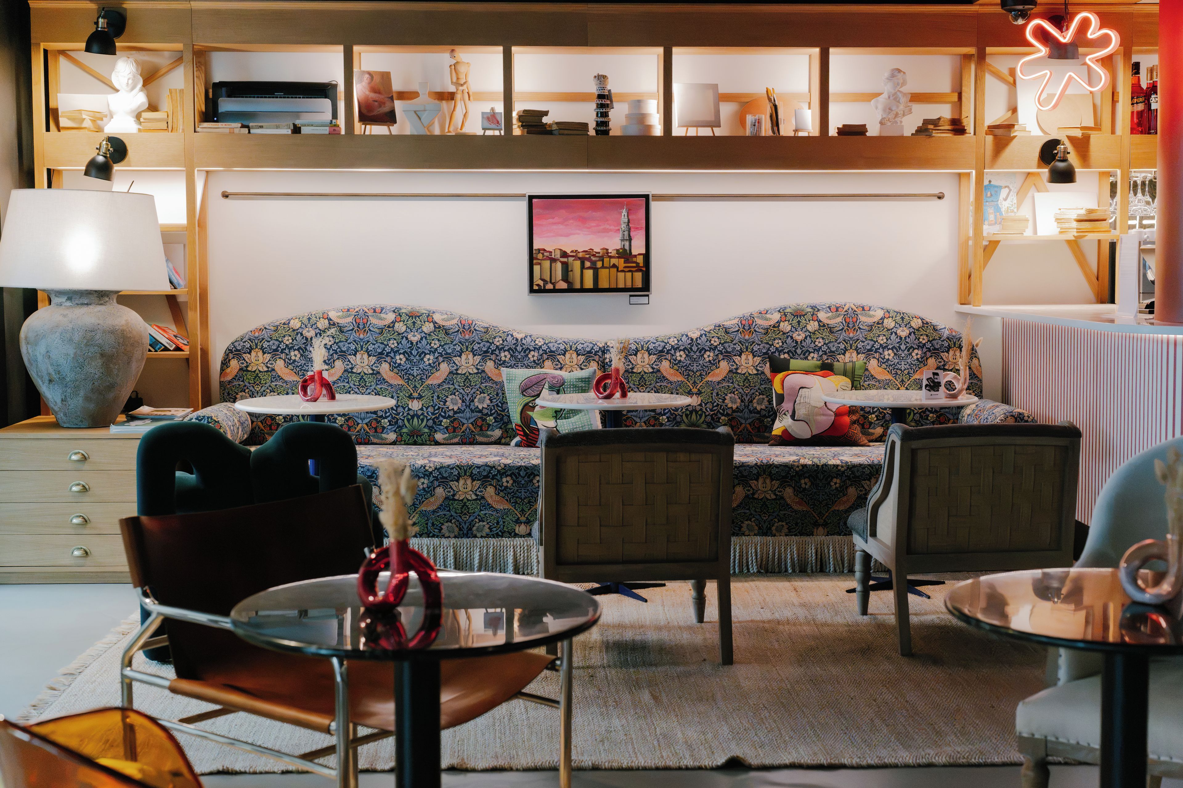 Ein gemütliches Wohnzimmer mit einer gemusterten Couch, einem Couchtisch und einem Bücherregal voller Bücher und Dekoration.